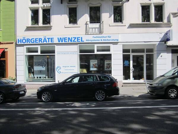Fachgeschäft für Hörgeräte und Hörberatung mit großer Fensterfront und geparkten Autos.
